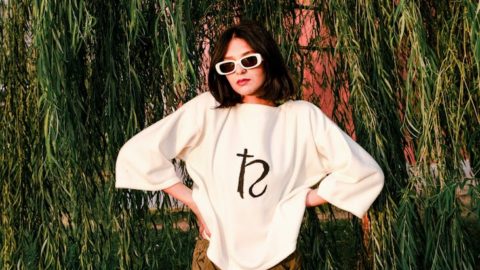 young woman in a trendy outfit standing on the background of a willow tree