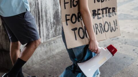 young woman and man walking in a protest holding a loudspeaker and a cardboard banner